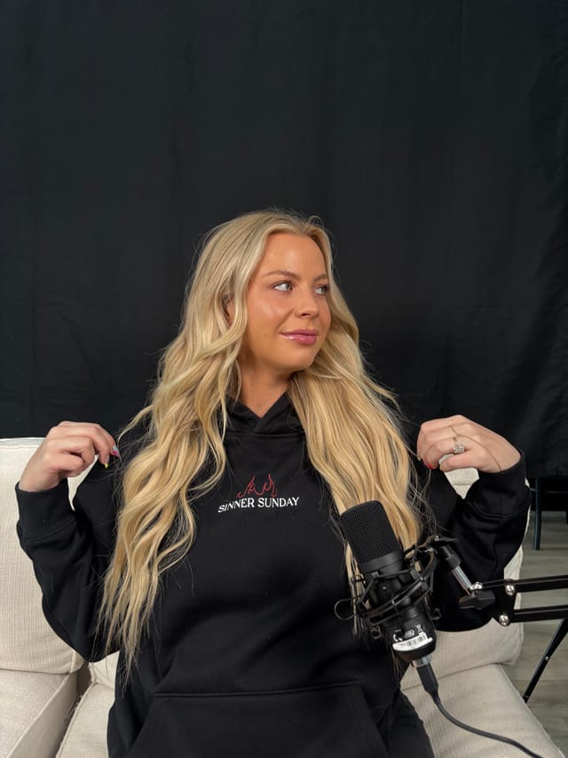 Maycie Neeley in a Sinner Sunday hoodie behind a studio microphone