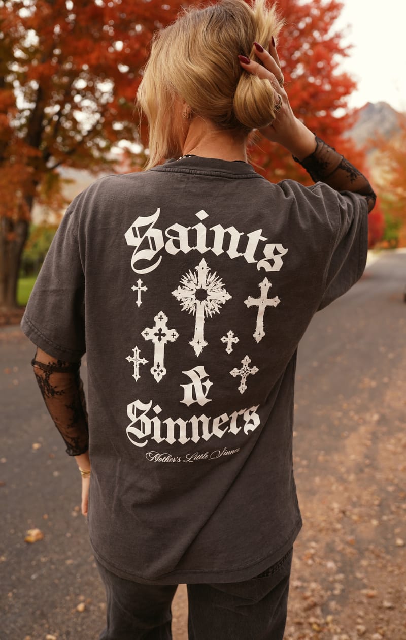 The back of the Saints & Sinners tee: SAINTS & SINNERS in white blackletter around a cluster of gothic crosses, Mother's Little Sinner in script beneath